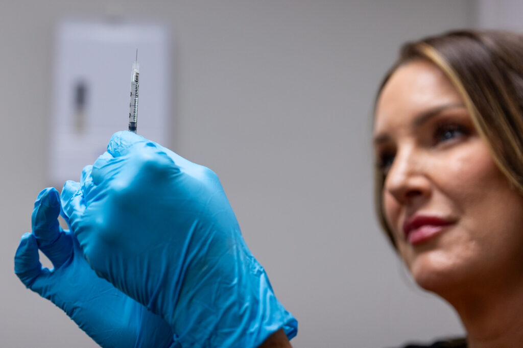 Medical professional wearing blue gloves holds syringe for administering bridal cosmetic treatments in Leawood