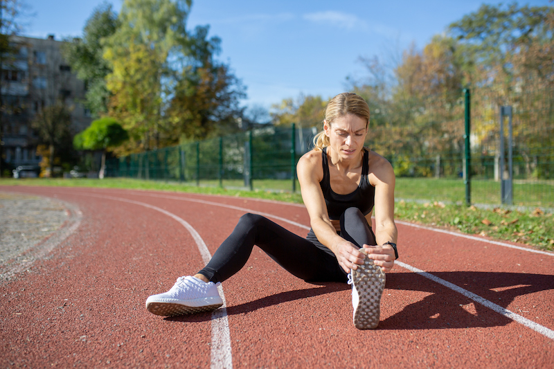 Focused female athlete stretching on outdoor running track on sunny day after having NAD+ in Kansas City.