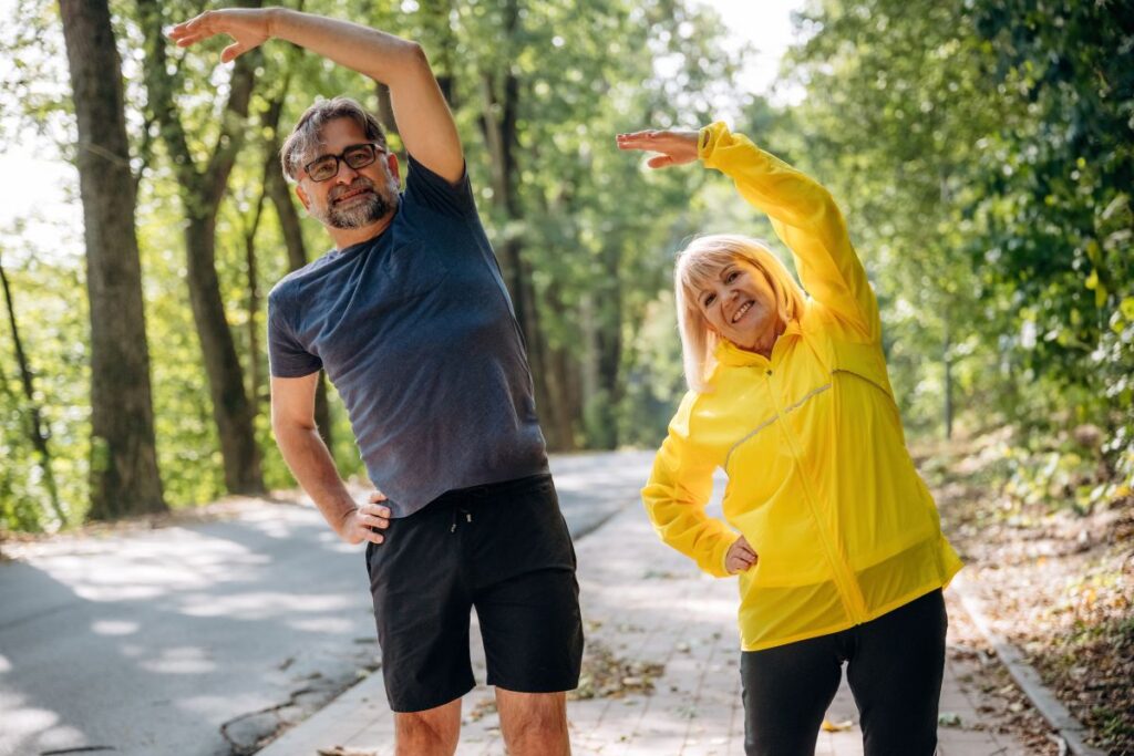 A mature couple on a jogging path stretching as part of how to improve longevity in Kansas City.