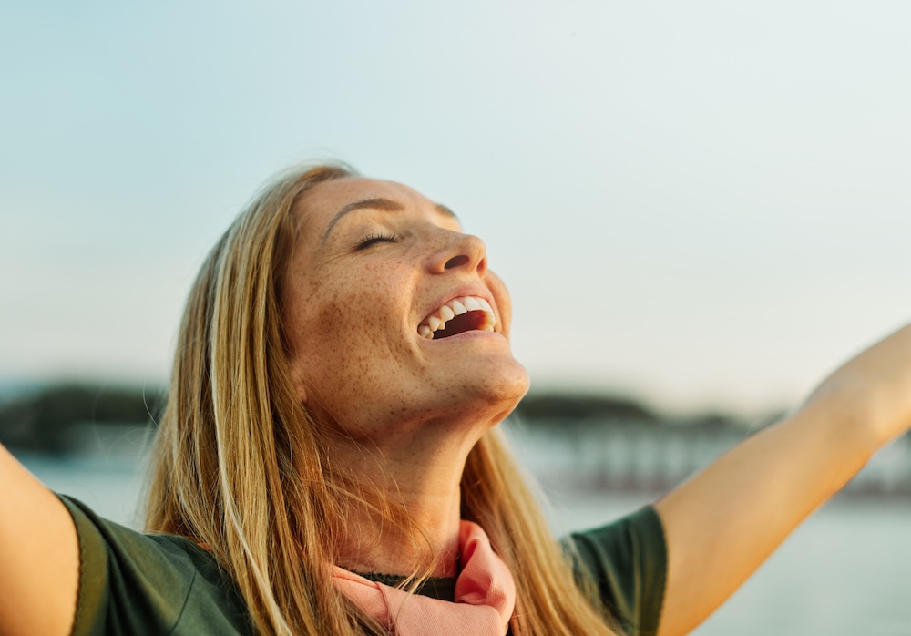 Woman smiles and holds arms up while standing outside because she's thrilled that she found the best treatment for vaginal dryness treatment in Leawood