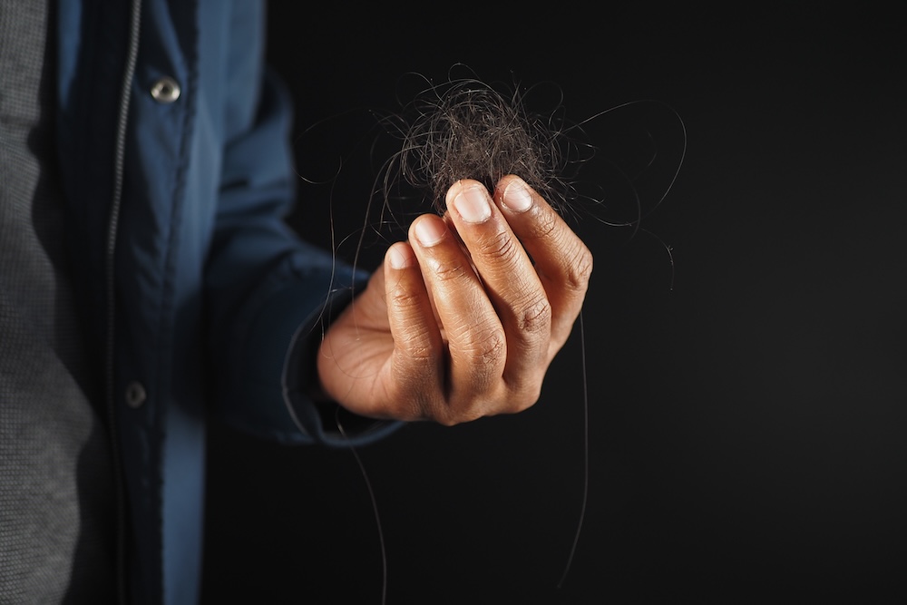 Person holds clump of hair in hands, a sign that it's time to visit the local wellness center and start a program for hair loss treatment in Leawood