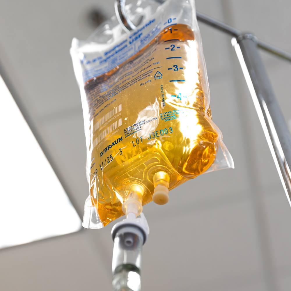 IV bag containing glutathione in Leawood hanging from hook and attached to tube that will deliver this coenzyme into patient's arm.
