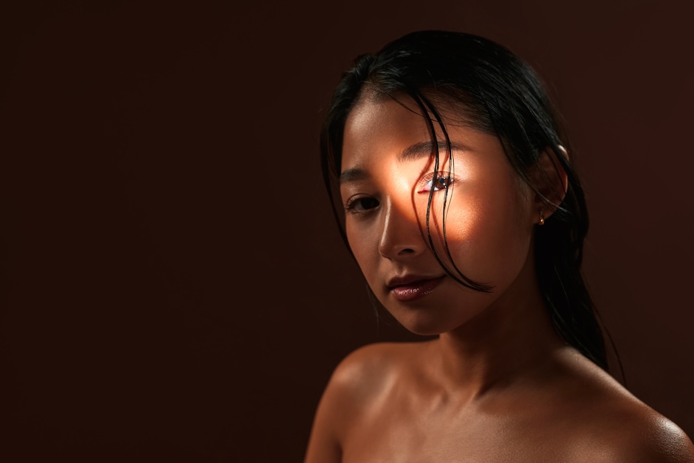Woman stands in dark room with a light shining on her eye. She has recaptured her glow with services for skin toning near Overland Park.