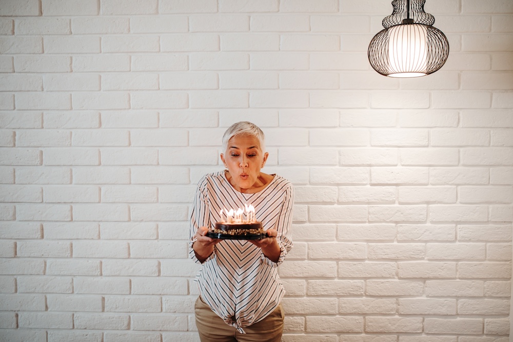 Senior woman proudly blowing out candles on her birthday cake and feeling confident after completing treatments for age spot removal in Leawood.