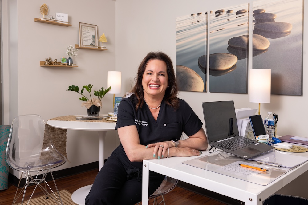 Woman smiles and sits at a desk with her laptop open, she's ready to greet patients and explain how you can achieve a V-shaped jawline contour with masseter Botox near Overland Park.