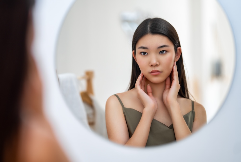 Woman looking in mirror and assessing her jawline, wondering if she should get treatment for masseter Botox near Overland Park.