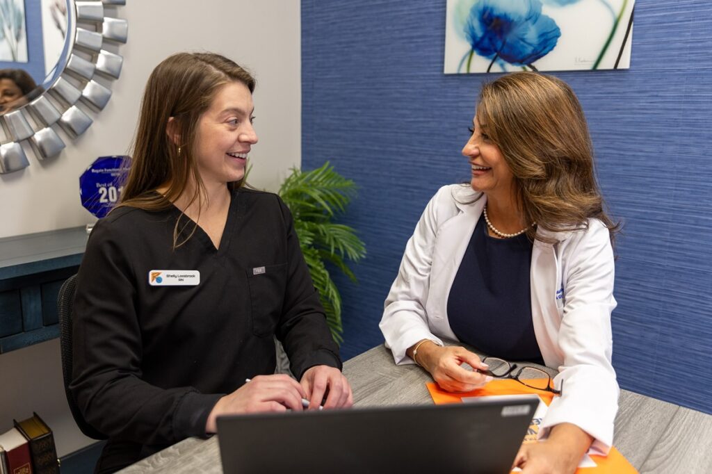 Provider and nurse look at each other over a laptop. They are discussing a comprehensive treatment plan for anti-aging in Leawood that focuses on internal health for outer beauty.