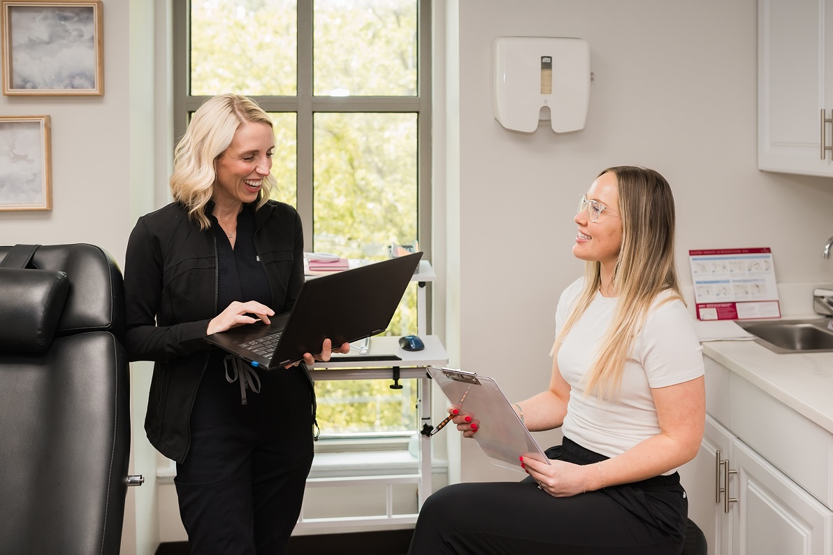 Provider and patient sitting in a treatment room discussing weight loss medications like phentermine in Kansas City. The provider is taking notes on her laptop regarding the patient's medical history and previous attempts at weight loss.