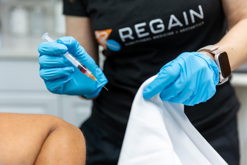 Provider wearing gloves administers hormone replacement therapy injections and prepares to administer them into patient's hip. This is a weekly treatment for anti-aging in Leawood that balances hormones like estrogen, testosterone, and progesterone.