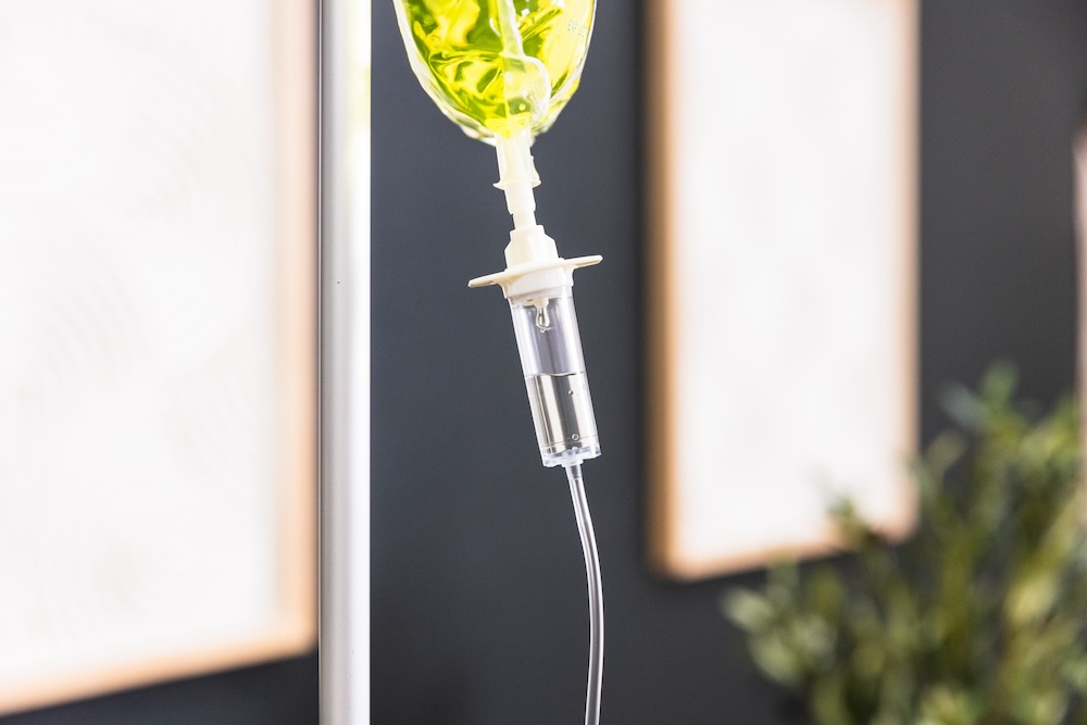 IV (intravenous) vitamin drip bag containing a vitamin and mineral blend fluid. The IV line is connected to a drip chamber, which is hanging from a pole in a medical spa where they offer vitamin drips in Kansas City.