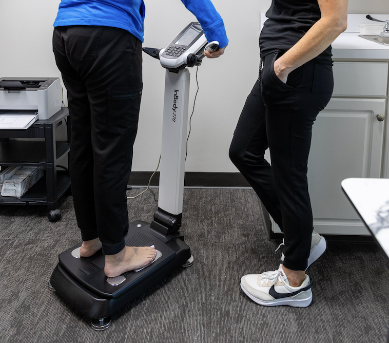 Woman standing on INBody body composition analysis to track her progress at a local weight loss clinic near Overland Park.