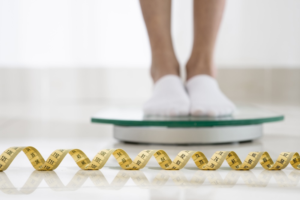 Person standing on a scale to track their progress with medical weight loss in Lawrence. In front of them, there is a curled tape measure laying on the ground.