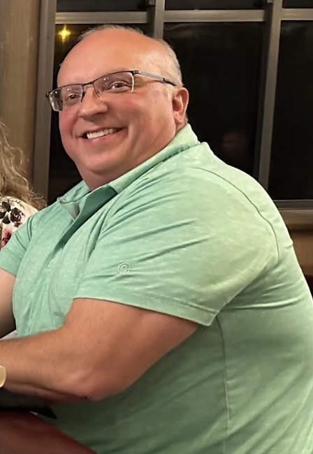Patient smiling and looking at the camera. He is wearing glasses and has his arms resting on a table. This is a before photo to document how he looked before starting weight loss injectables in Leawood.