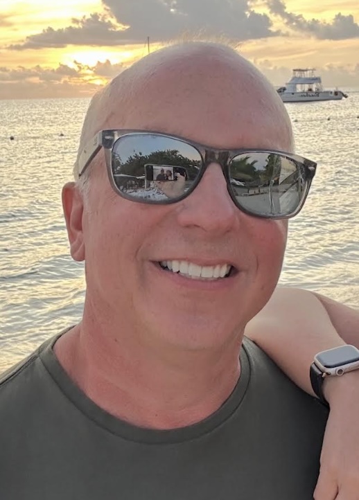 Patient smiling for the camera after he reached his goals with weight loss injectables. He's standing on a sunny beach, wearing sunglasses and smiling confidently for the camera.